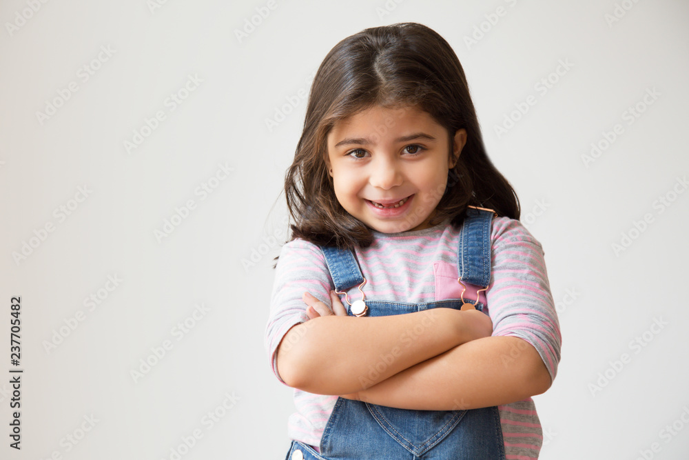 Cheerful Hispanic child standing with crossed arms. Cute little girl posing in casual clothing. Isolated on white. Childhood concept Cheerful Hispanic child standing with crossed arms. Cute little girl posing in casual clothing. Isolated on white. Childhood concept