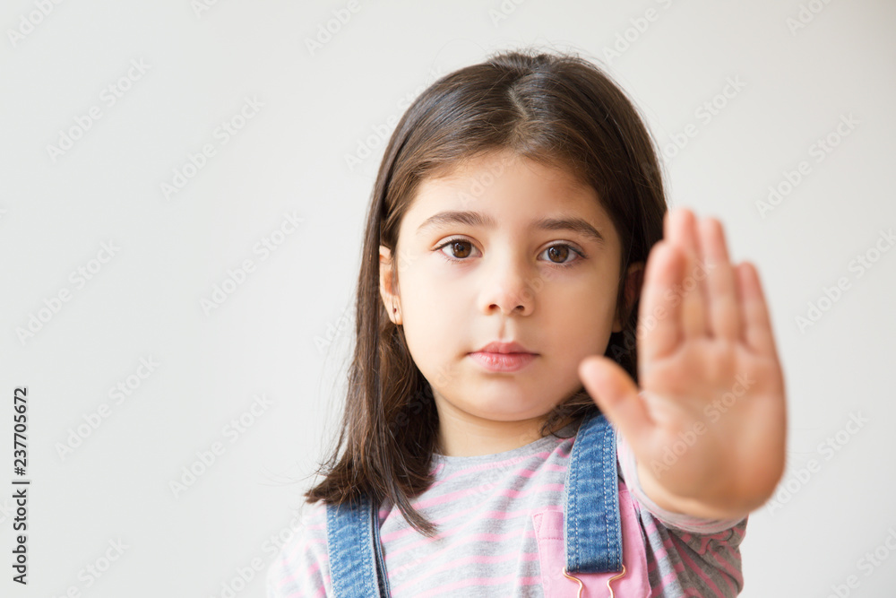 Little serious kid gesturing forbidden with one hand. Adorable Hispanic little girl making stop gesture. Isolated on white. Prohibition concept Little serious kid gesturing forbidden with one hand. Adorable Hispanic little girl making stop gesture. Isolated on white. Prohibition concept