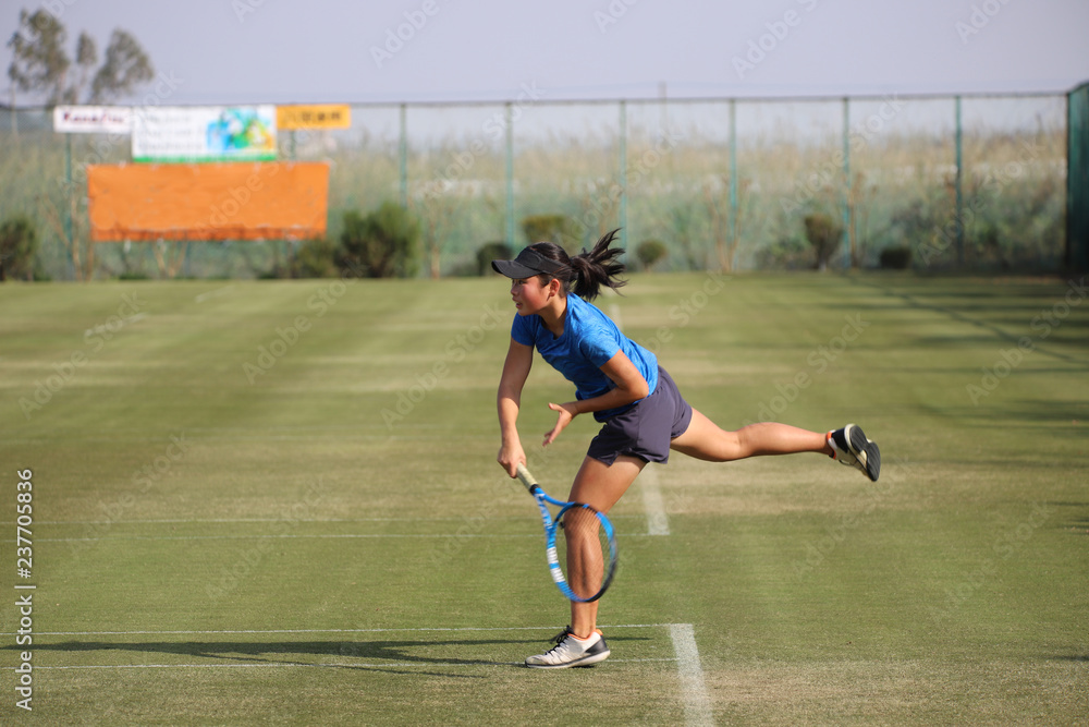 Fototapeta premium 天然芝のコートでサーブ打つジュニアテニスプレイヤー