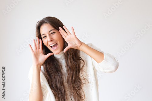 Excited Hispanic girl shouting about sale and discount. Cheerful Latin young woman holding hands near mouth and yelling. Isolated on white. Advertising concept