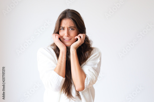 Frightened Hispanic girl with hands nead face looking at camera. Beautiful stressed young woman. Isolated on white with copy space. Stress concept