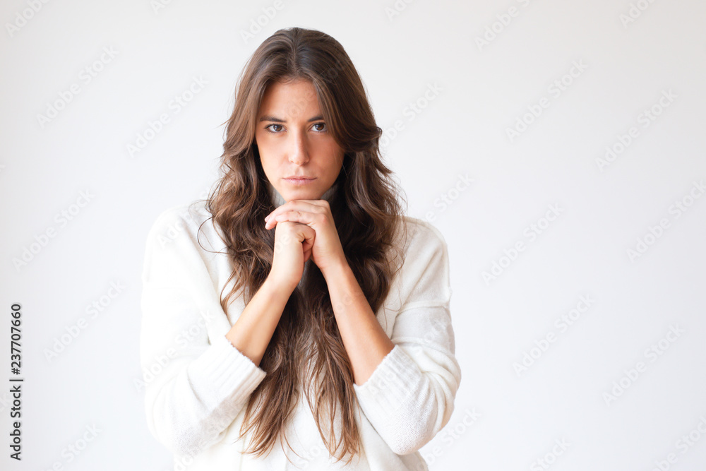 Pensive young woman holding chin and looking at camera. Beautiful thoughtful Hispanic girl in white sweater. Isolated on white. Thinking concept Pensive young woman holding chin and looking at camera. Beautiful thoughtful Hispanic girl in white sweater. Isolated on white. Thinking concept
