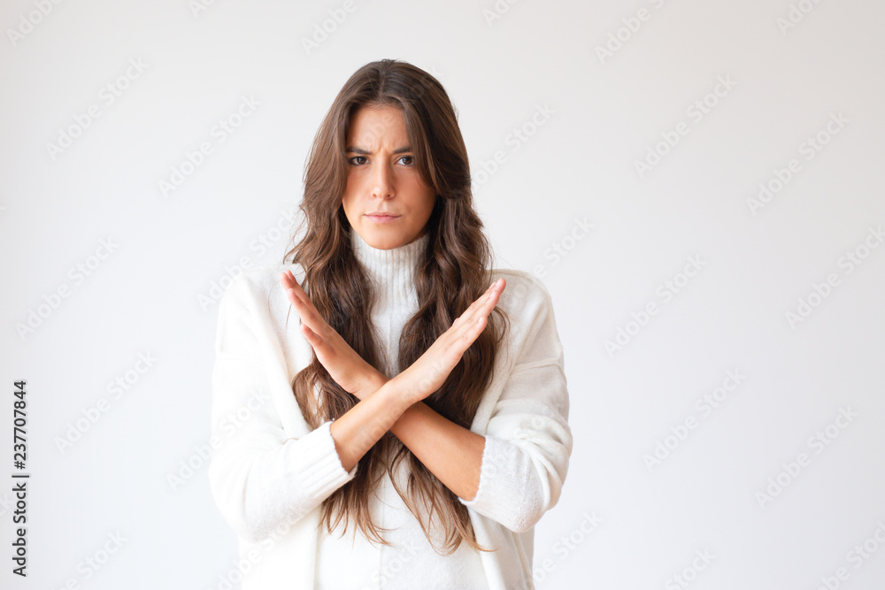 Fototapeta premium Serious young woman showing forbidden symbol. Attractive girl with ban gesture looking at camera. Isolated on white. Prohibition concept