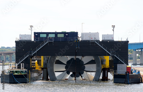  Giant tidal turbine docked in a harbor. It is held in a ship designed to hold and transport it. Sky is overcast. Walkways on ship give sense of scale. Identifying marks removed. Room for text. photo