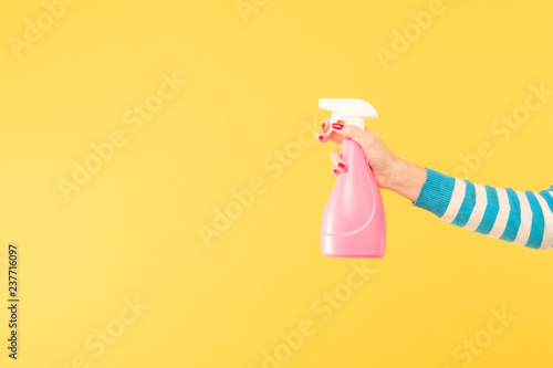 female hand holding bright pink cleanser sprayer on yellow background. cleaning housework and household chores photo