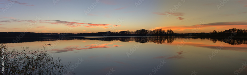 Orange and pink sunset sky panorama over a rural german countryside with a peaceful lake with a row of trees, reflectied in the calm waters. Orange and pink sunset sky panorama over a rural german countryside with a peaceful lake with a row of trees, reflectied in the calm waters.