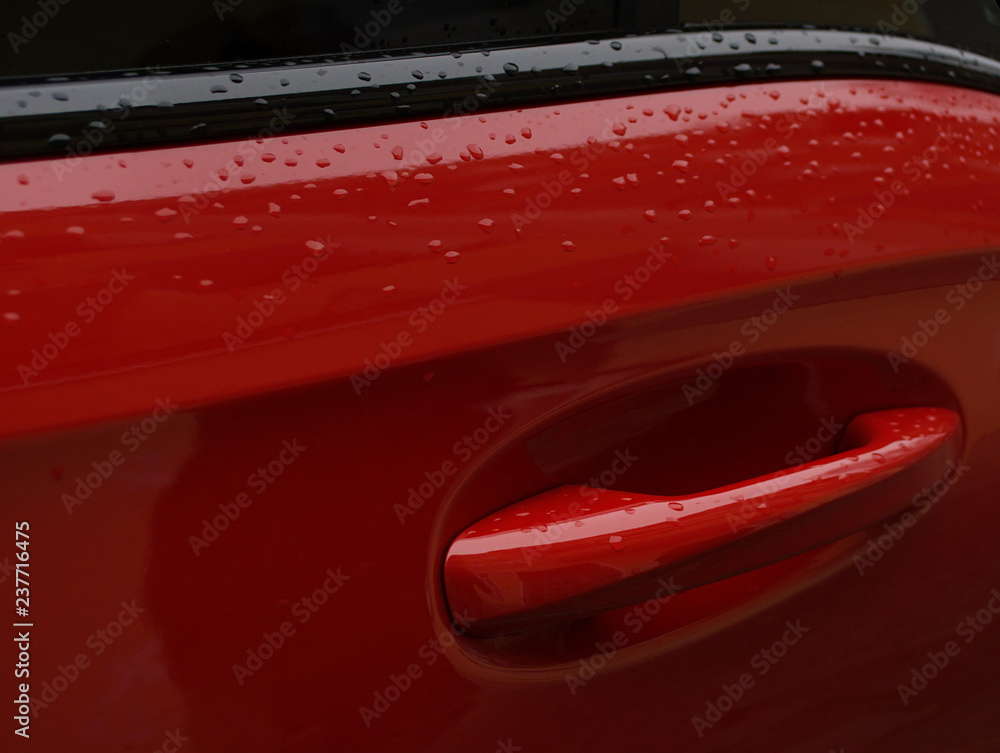 Closeup of a modern red car door handle covered with rain drops