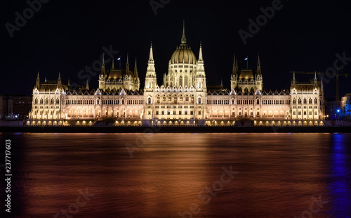 Hungarian Parliament building, in Budapest, at night. The building is lit up, and the Danube is flowing smoothly in front of it.