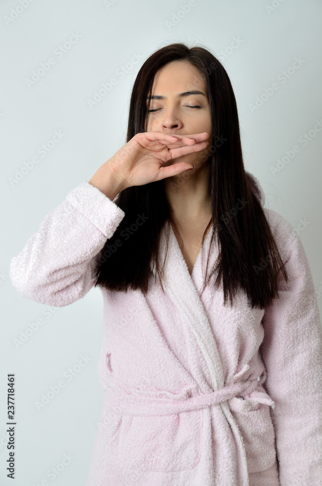 Young female wearing dressing-gown with white background. Awaking in the morning, stretching and yawning. Young female wearing dressing-gown with white background. Awaking in the morning, stretching and yawning.