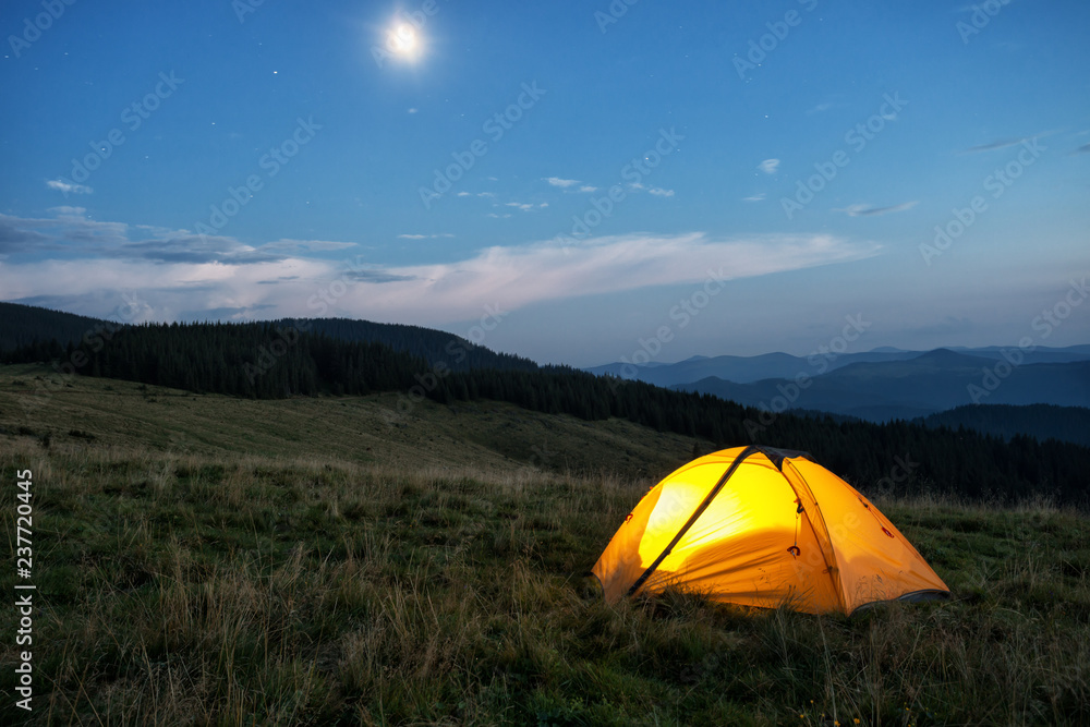 Illuminated orange tent in mountains at dusk