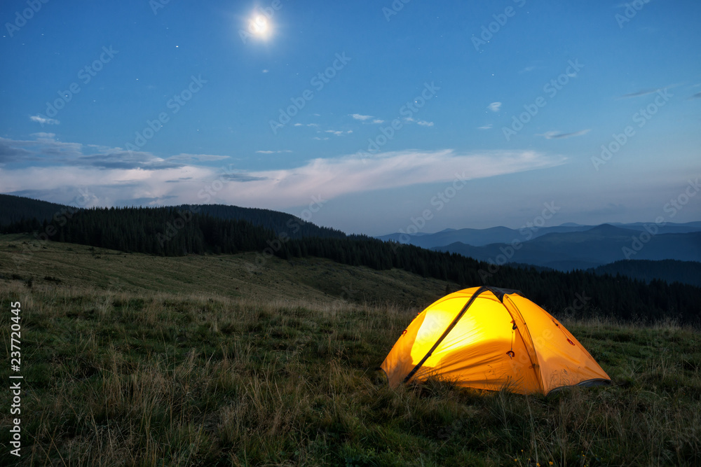Illuminated orange tent in mountains at dusk Illuminated orange tent in mountains at dusk