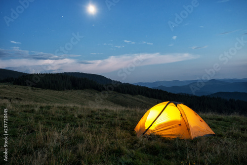 Illuminated orange tent in mountains at dusk