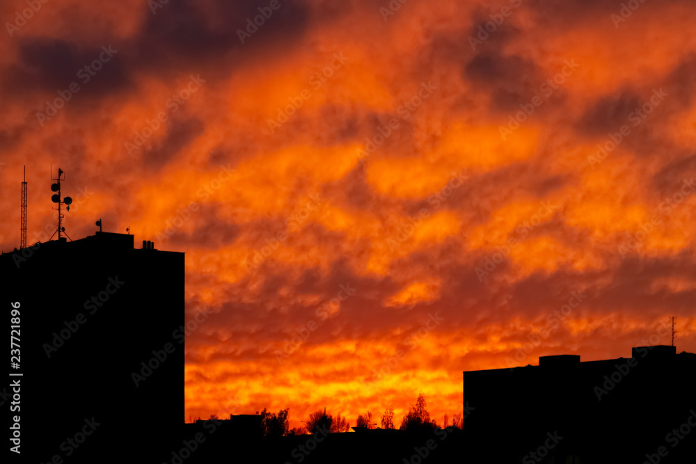 Silhouettes of urban landscape during dramatic sunset with yellow and red fully cloudy sky