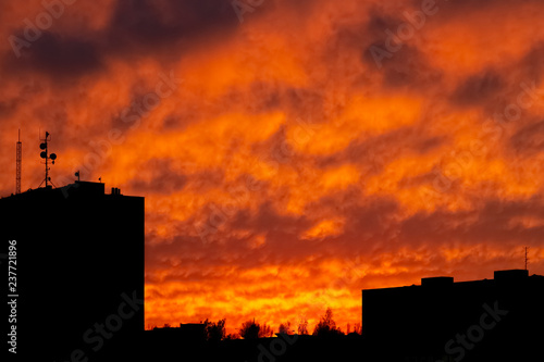 Silhouettes of urban landscape during dramatic sunset with yellow and red fully cloudy sky