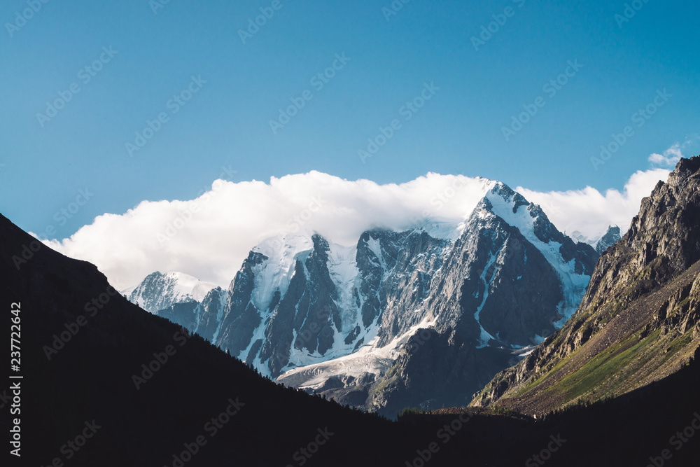 Amazing glacier under blue sky. Mountain range with snow. Huge cloud on giant wonderful snowy mountains. Atmospheric minimalist moody landscape of majestic nature of highlands in matte tones.