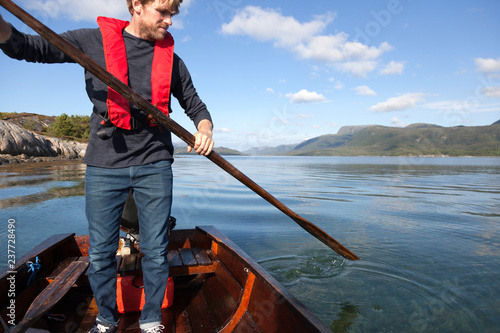 Mature man standing up to use oar in rowing boat, Aure, More og Romsdal, Norway photo