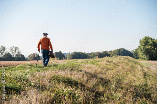 Senior man carrying traveling bag, walking in the fields
