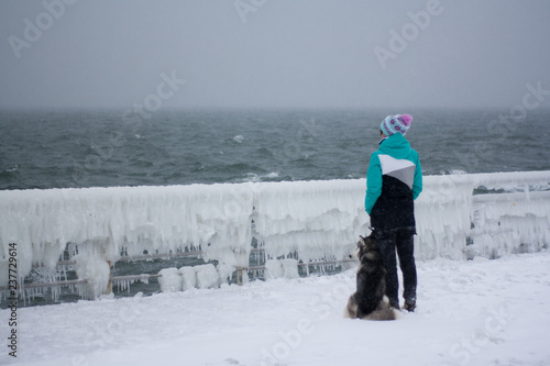 Young woman having fun with husky in the snow on the beach near the sea. Snow weather.