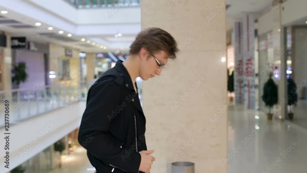 Portrait of a modern young man in glasses and leather jacket in a large modern shopping center. Shopping. Portrait of a modern young man in glasses and leather jacket in a large modern shopping center. Shopping.