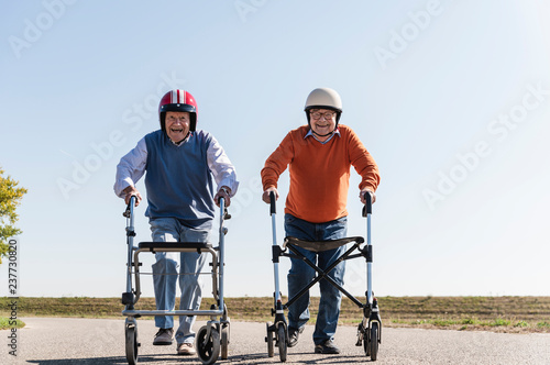 Two old friends wearing safety helmets, competing in a wheeled walker race photo