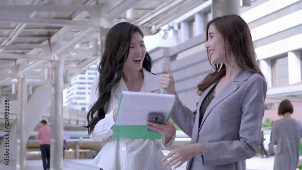 Two Businesswomen talking new startup project and smiling happily in city centre Thailand. Business Meeting concept. SLOW MOTION Two Businesswomen talking new startup project and smiling happily in city centre Thailand. Business Meeting concept. SLOW MOTION