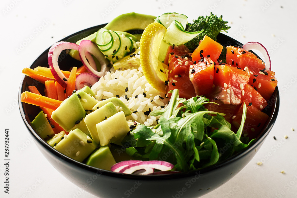 poke bowl with salmon, avocado, cucumber, arugula, broccoli, rice, carrot and sweet onions isolated over white background. side view