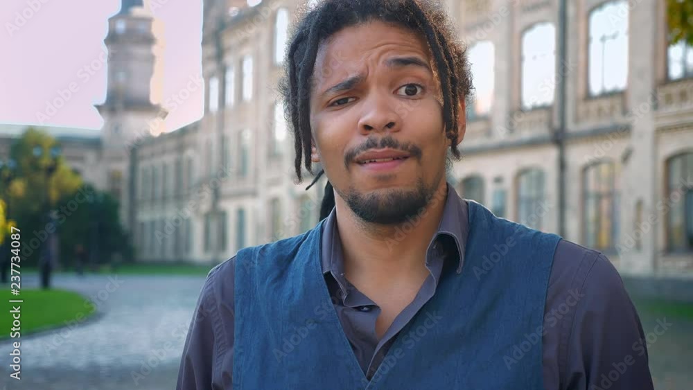 Portrait of attractive African-American student with dreadlocks negatively waving his head on university background. Portrait of attractive African-American student with dreadlocks negatively waving his head on university background.