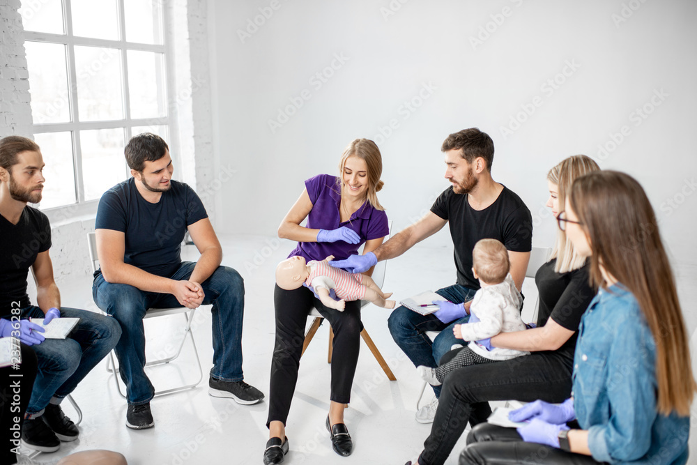 Group of people during the first aid training with instructor showing on manikin how to do artificial respiration for the baby Group of people during the first aid training with instructor showing on manikin how to do artificial respiration for the baby