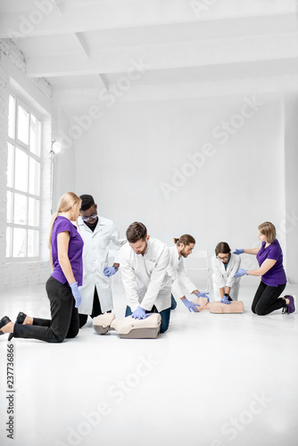 Group of young medics practising to make artificial breathing with medical dummies during the first aid training in the white room