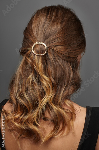 Close up isolated portrait of a young lady with brown ombre hair colour. The back view of the girl with half-up hairstyle, adorned with golden open oval barrette. Posing against the grey background.