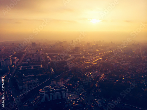 Aerial panorama of dramatic sunset over big city in evening twilight fog or haze, drone view cityscape