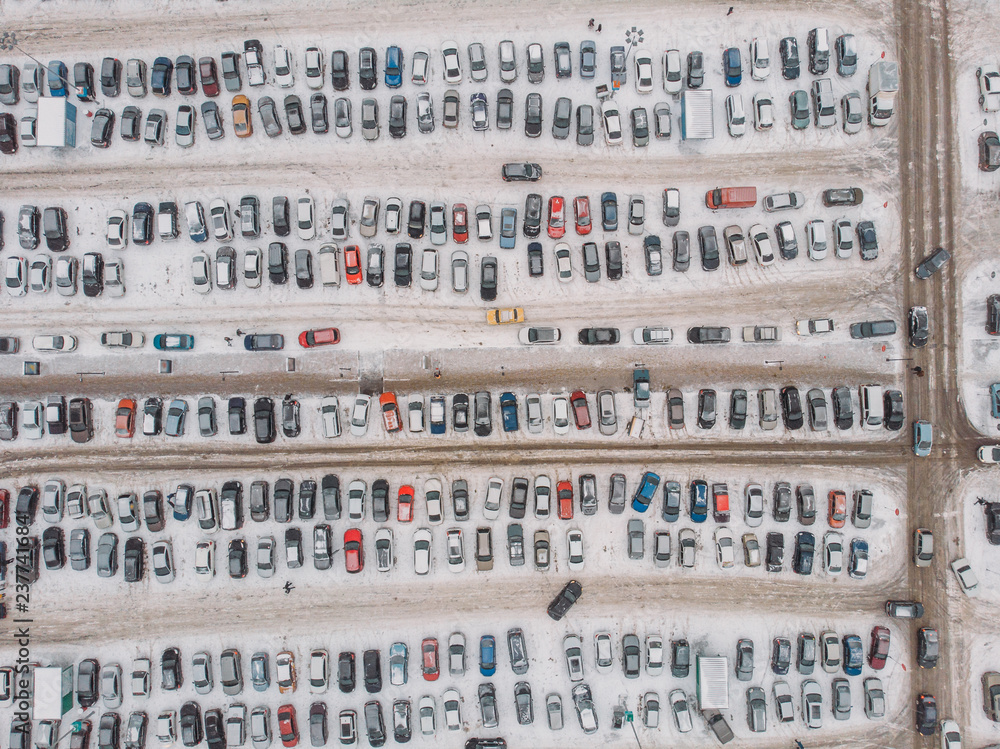 Parking lot with many cars near mall or shopping center in winter with snow, aerial view, drone photo