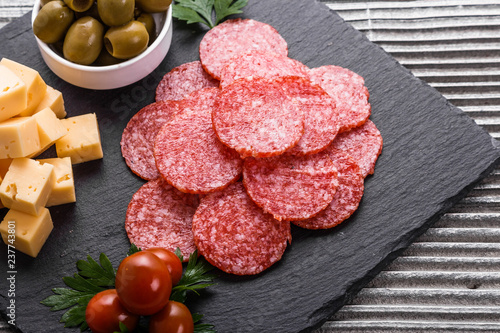 Canvastavla delicious sliced salami on a stone plate wooden background