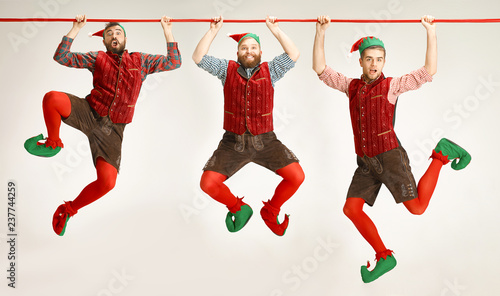 The happy smiling friendly men dressed like a funny gnome or elf hanging on an isolated gray studio background. The winter, holiday, christmas concept photo