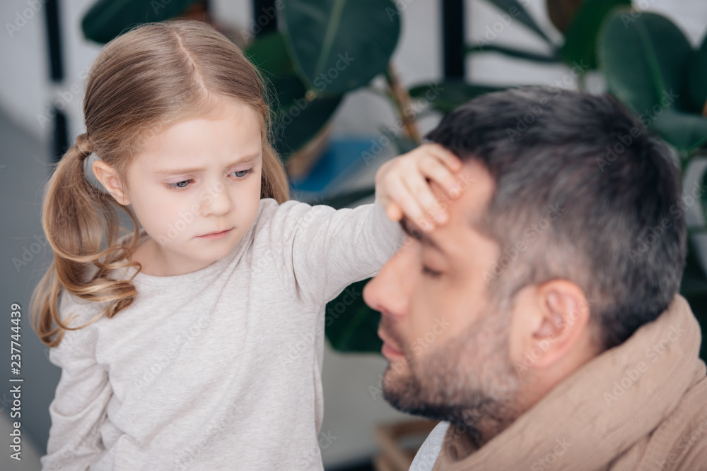 Fototapeta premium selective focus of adorable daughter touching sick father forehead and checking temperature in bedroom