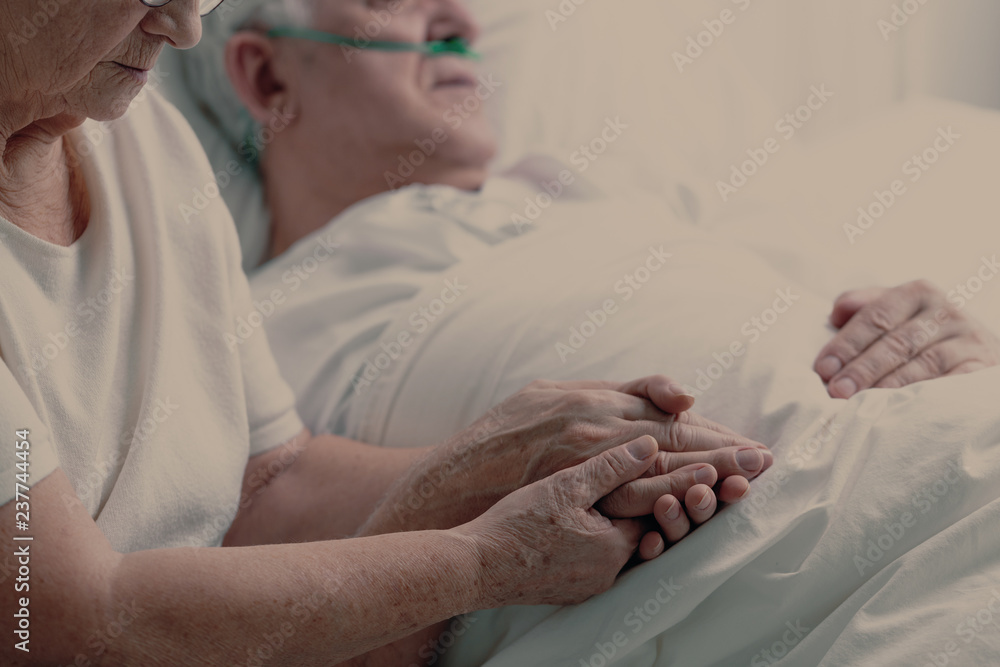 Senior man with lung cancer laying in hospice bed supporting by his elderly wife, photo with copy space Senior man with lung cancer laying in hospice bed supporting by his elderly wife, photo with copy space