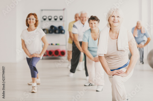 Smiling senior woman with towel exercising during yoga classes for elderly people