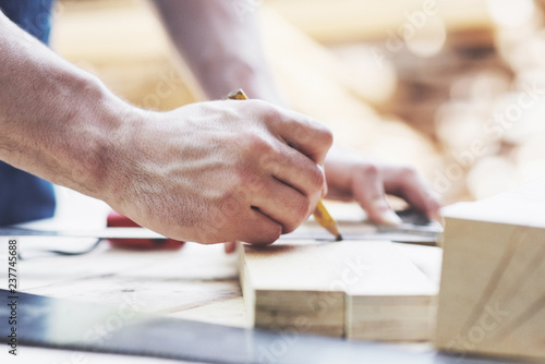 A carpenter in working clothes and a small business owner takes a wooden board with a ruler and pencil.