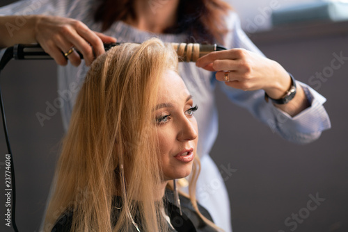 beautiful adult blonde client sits in a chair while a hairdresser master in the salon does her hair with a corrugation and a Perm
