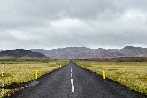 The way forward. Iceland road trip. Empty straight asphalt road, green fields and a distant mountain range on a cloudy summer day. Landscape of Reykjanes Peninsula