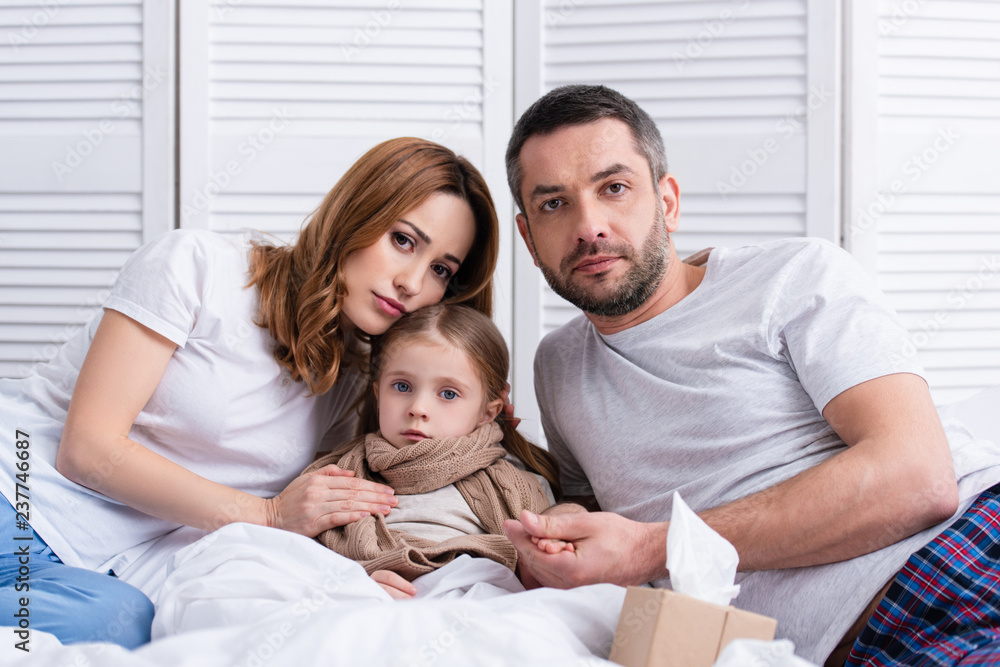 parents taking care of sick daughter in bedroom and looking at camera parents taking care of sick daughter in bedroom and looking at camera