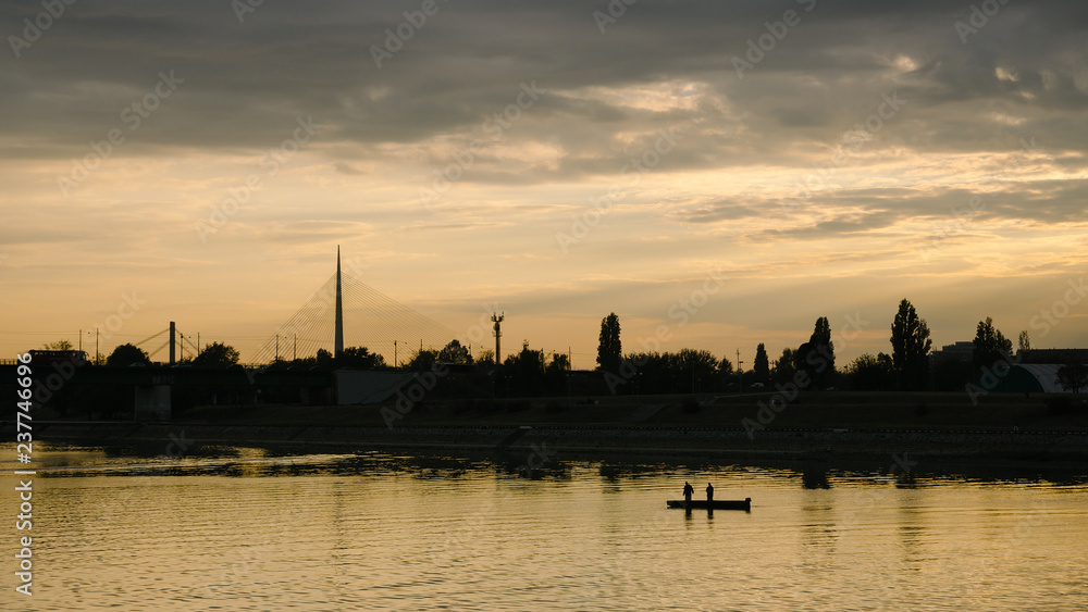 Silhouette of two men on the boat on a river