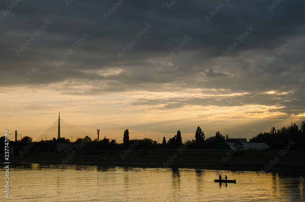 Silhouette of two men on the boat on a river