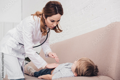 Bild auf Leinwand pediatrist palpating sick boy stomach on sofa in living room