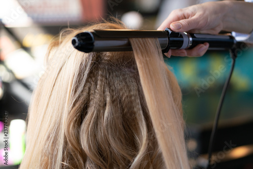 beautiful adult blonde client sits in a chair while a hairdresser master in the salon does her hair with a corrugation and a Perm