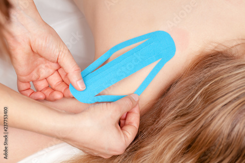 Physical therapist applying kinesiology tape to tween girl shoulder - Kinesiotaping concept photo