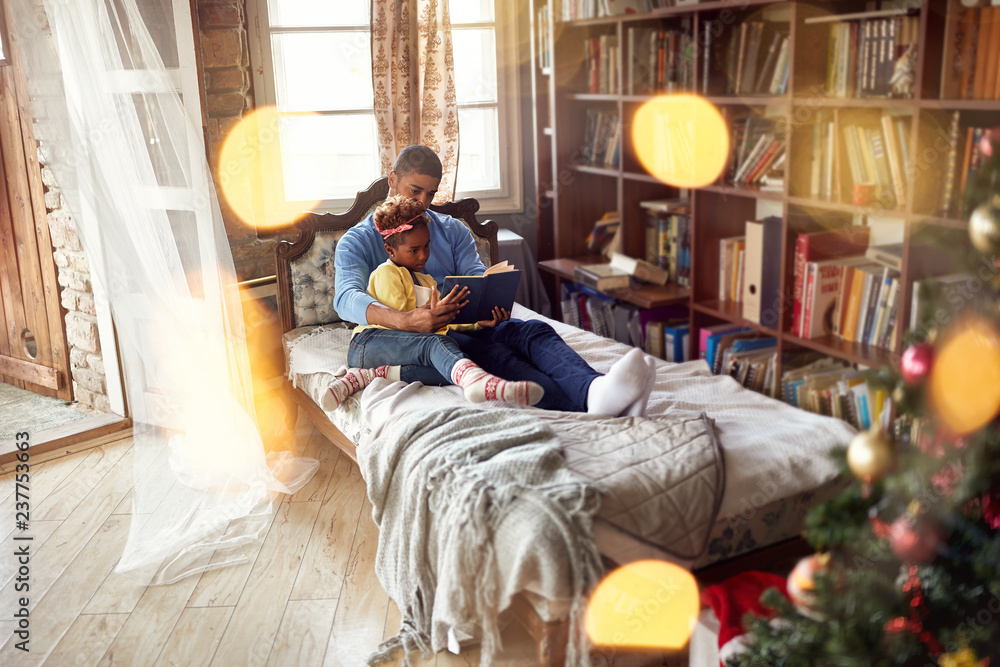 African American father and daughter reading fairy tales for the Christmas holidays.