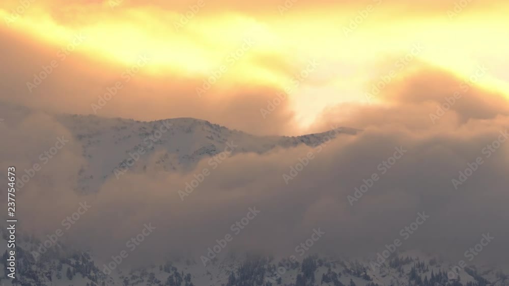 Low foggy clouds moving over snow covered mountains during colorful sunrise in Utah. Low foggy clouds moving over snow covered mountains during colorful sunrise in Utah.