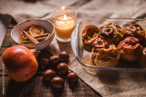 Roasted apples in a glass tray with chestnuts, candle, cinnamon, orange and pomegranate