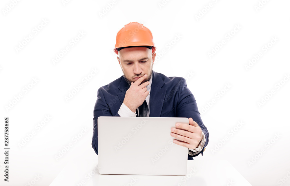 A tired constructor businessman in an orange helmet looks at the laptop screen and studies the construction project. Sits at the table and drinks coffee, nervous A tired constructor businessman in an orange helmet looks at the laptop screen and studies the construction project. Sits at the table and drinks coffee, nervous